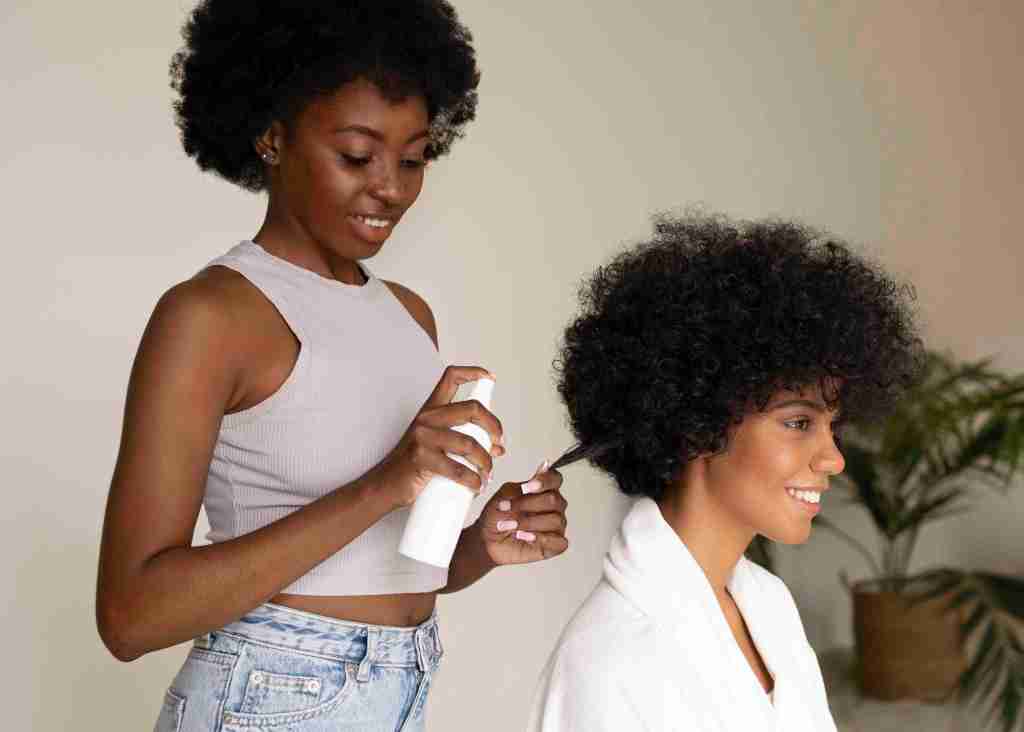Black hairstylist gently caring for a client's natural curls in a salon, highlighting expert natural hair care and the importance of cultural connection through styling.