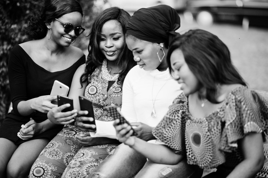 A group of Black friends having a travel planning conversation , looking at their phones showcasing strong communication as part of Black group travel tips for stress-free trips.