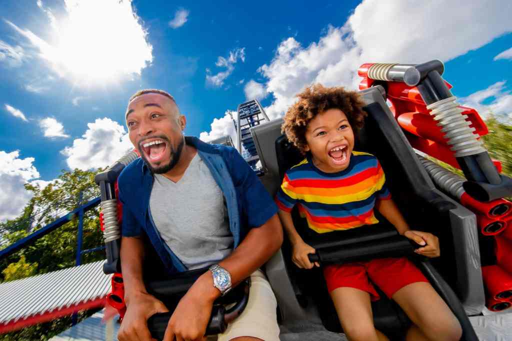 Father and Son smiling riding a colorful roller coaster in Orlando, Florida, highlighting a kid friendly and family-friendly attraction.